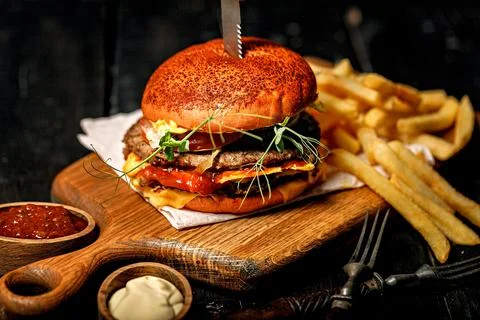 Appetizing double beef burger and a serving of fries on a wooden cutting boar Stock Photos