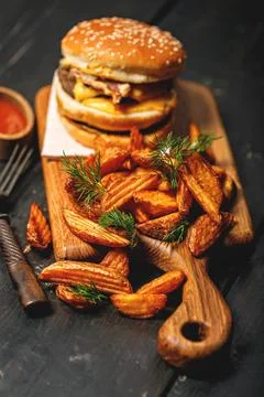 Appetizing double beef burger and a serving of fries on a wooden cutting boar Stock Photos
