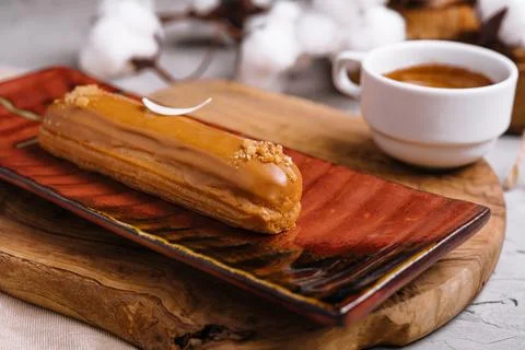 Appetizing eclair with caramel glaze and peanuts and coffee Stock Photos