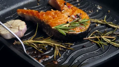 Appetizing fish steak is fried in a pan. pouring hot butter over the fish from Stock Footage 198893256