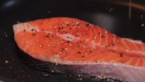 Appetizing fish steak is fried in a pan. Sprinkling grated pepper mix over Stock Footage 309563656