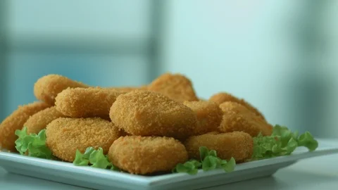 Appetizing freshly prepared breaded chicken nuggets fall into a white plate Stock Footage 116875055