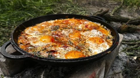 Appetizing fried eggs with herbs bubbling in large cast iron pan Stock Footage 337203631