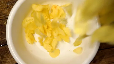 Appetizing fried yellow potato chips falling into a plastic bowl Stock Footage 139413751