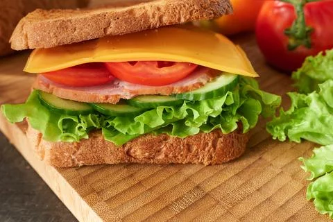 An appetizing ham, cheese and vegetable sandwich on a wooden board. Stock Photos