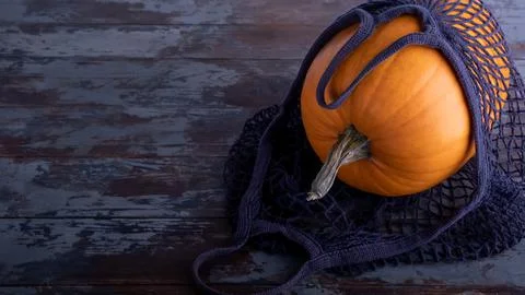 An appetizing large orange pumpkin lies on its side in a blue mesh shopping b Stock Photos