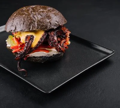 Appetizing marinated octopus burger on a black tray Stock-Fotos