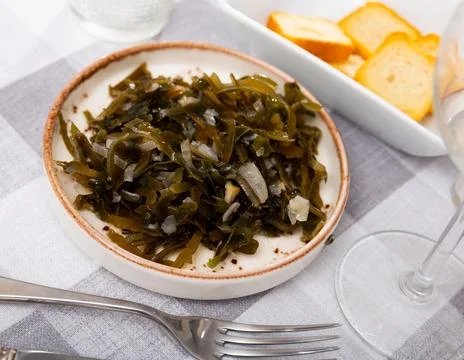 Appetizing marinated seaweed salad with onion served in plate with cutlery and Stock Photos