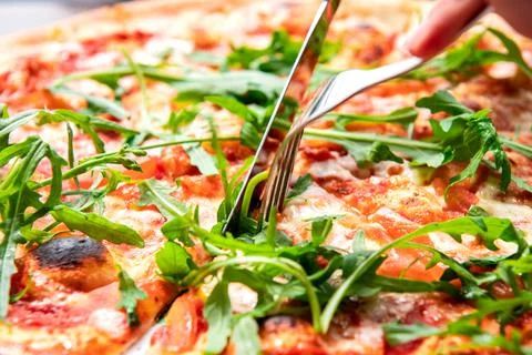 Appetizing pizza in a cafe. The visitor cuts the pizza with a knife and fork  Stock Photos