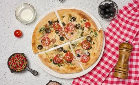 Appetizing pizza cut into pieces on a round white plate with tomatoes, oliv.. 스톡 사진