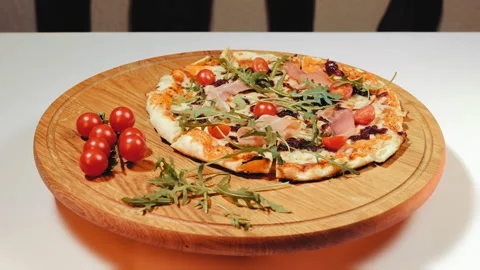 Appetizing pizza rotating and lying on a wooden board with cherry tomatoes Stock Footage 252290556