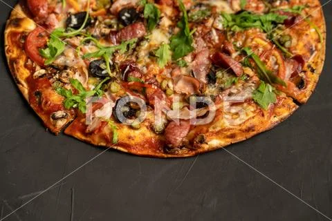 Appetizing pizza with smoked sausages bacon meat tomato cheese arugula on bla Stock Photos