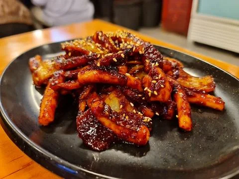 Appetizing red glazed squid pieces with sesame seeds are arranged on a black  Фото