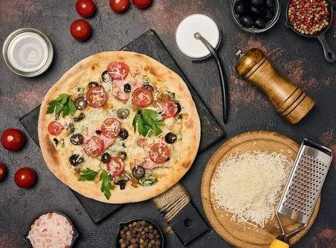 Appetizing round pizza on a black board surrounded by cherry tomatoes, oliv.. 스톡 사진