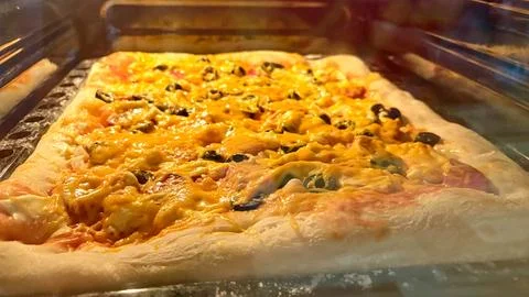 An appetizing shot of a large rectangular pizza being baked inside an oven. Stock Photos