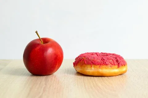 An apple and a donut on the table. concept of choosing healthy food and Stock Photos