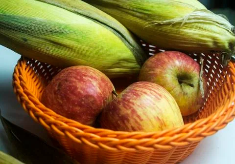 Apple and leafed corn in orange plastic fruit basket 库存照片