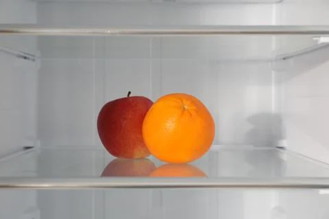 Apple and orange on shelf inside modern refrigerator Fotos de archivo