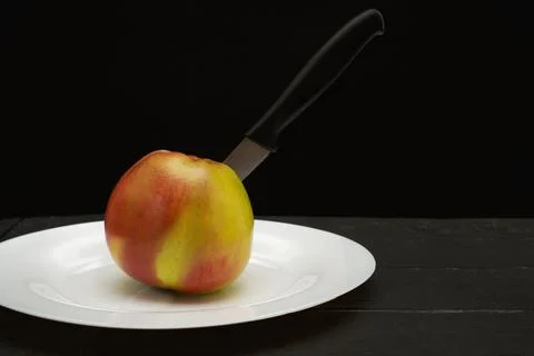 Apple on a black background with a knife inside on a white plate 스톡 사진