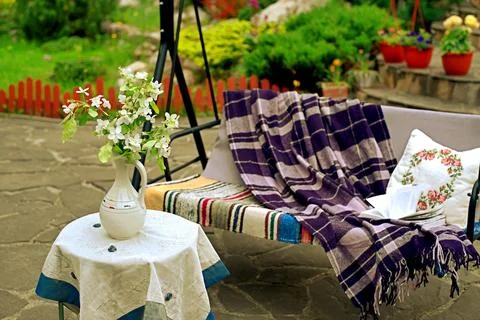 Apple blossoms on a table in front of a sofa swing in the courtyard of a co.. Stock Photos