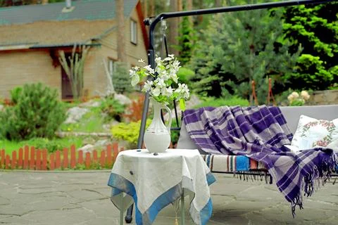 Apple blossoms on a table in front of a sofa swing in the courtyard of a co.. Stock Photos