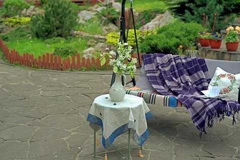 Apple blossoms on a table in front of a sofa swing in the courtyard of a coun Stock Photos