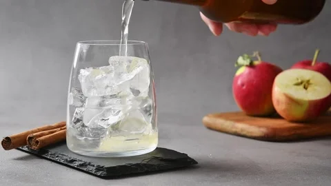 Apple cider pours over ice in glass to begin preparation of apple cider cold Stock Footage 345557278