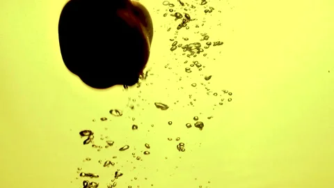 An apple falls into the water under backlighting, bubbles rise from the water 库存影片 146643017
