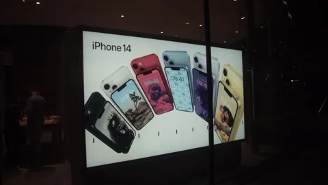 An Apple iPhone 14 advertisement is displayed on a screen at a shopping mall Vídeos de archivo 250414720