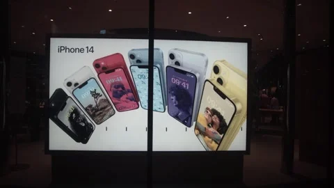 An Apple iPhone 14 advertisement is displayed on a screen at a shopping mall Stock Footage 250414734