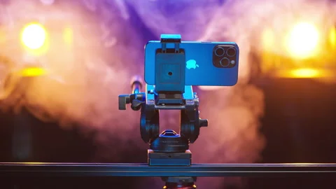 Apple iPhone 15 Pro Max on tripod stand with spotlights in background 4K Stock Footage 260064753