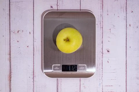 An apple lies on a digital kitchen scale on a table of light boards. Stock Photos