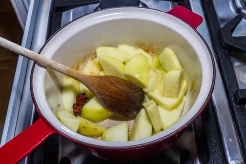 Apple in pan about to be cooked with apple sauce with spoon on hob. Stock Photos
