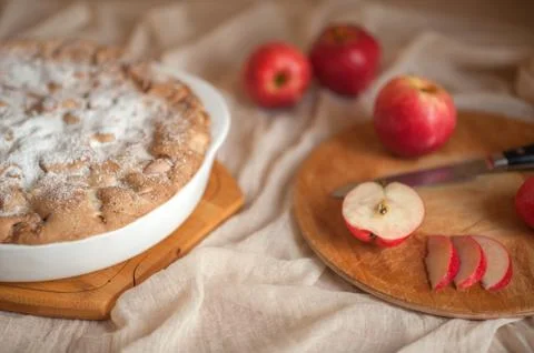 Apple pie on a neutral background, apples lie nearby. Stock Photos