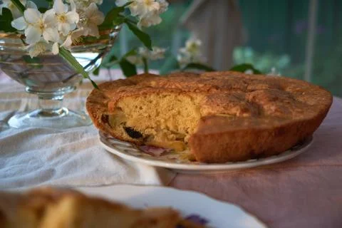 Apple pie is in the plate on the table next to the vase and flowers Photos