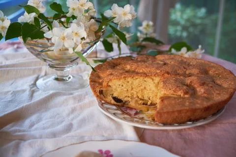 Apple pie is in the plate on the table next to the vase and flowers Stock Photos