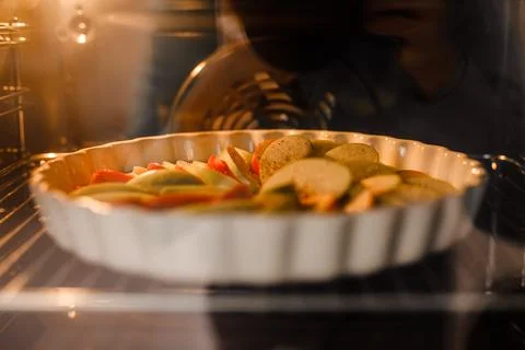 An apple pie in a white dish is baking inside the oven Stock Photos
