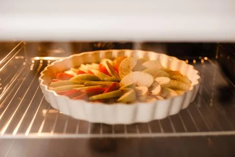 An apple pie in a white dish is baking inside the oven Stock Photos