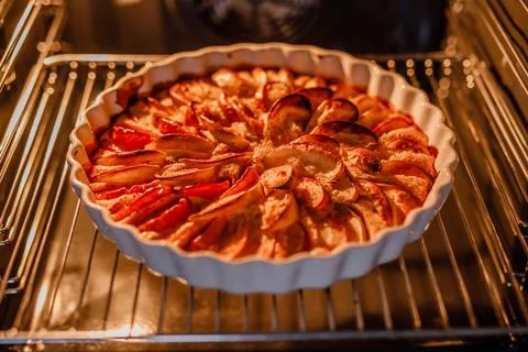 An apple pie in a white dish is baking inside the oven Stock Photos