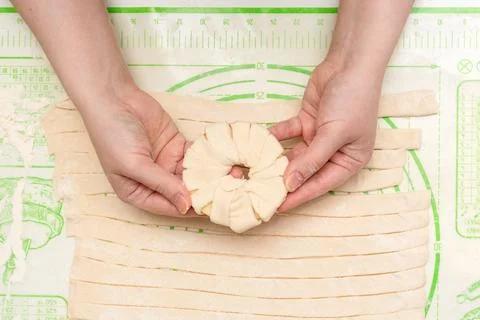 An apple ring wrapped in dough in the hands of a young woman. Stock Photos
