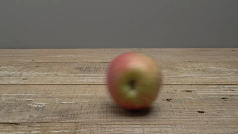 An apple is rolling on a wooden surface on a gray background. Видео 266125334