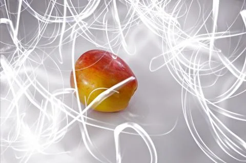 An apple sitting on a white surface with light painting streaks above and aro Stock Photos