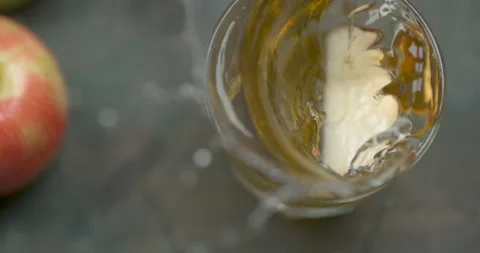 Apple slice falling in a tall glass of apple juice, on a wooden table decorated Stock Footage 199462160