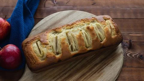 Apple sponge cake on a kitchen board on a dark wooden background. Copy space. Stock Photos