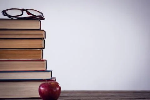 Apple by stack of book with eyeglass at table Stock Photos