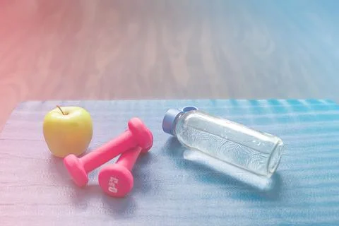 An apple, two red dumbbells and a bottle of water on a blue mat. Stock Photos