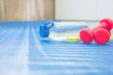 An apple, two red dumbbells and a bottle of water on a blue mat. Home workout Stock Photos