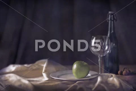 Apple, wine glass and bottle on tablecloth Stock Photos