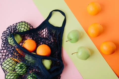 Apples and oranges in a blue string bag on a colored background. Fruits in a 스톡 사진
