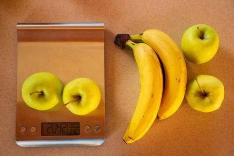 Apples on a digital kitchen scale and beside are bananas and apples Stock Photos